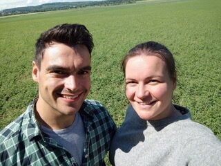 Du siehst zwei fröhliche Menschen vor einem grünen Feld-perfekte Kulisse für Öle und Saaten von Ölacker bei sonnigem Wetter.